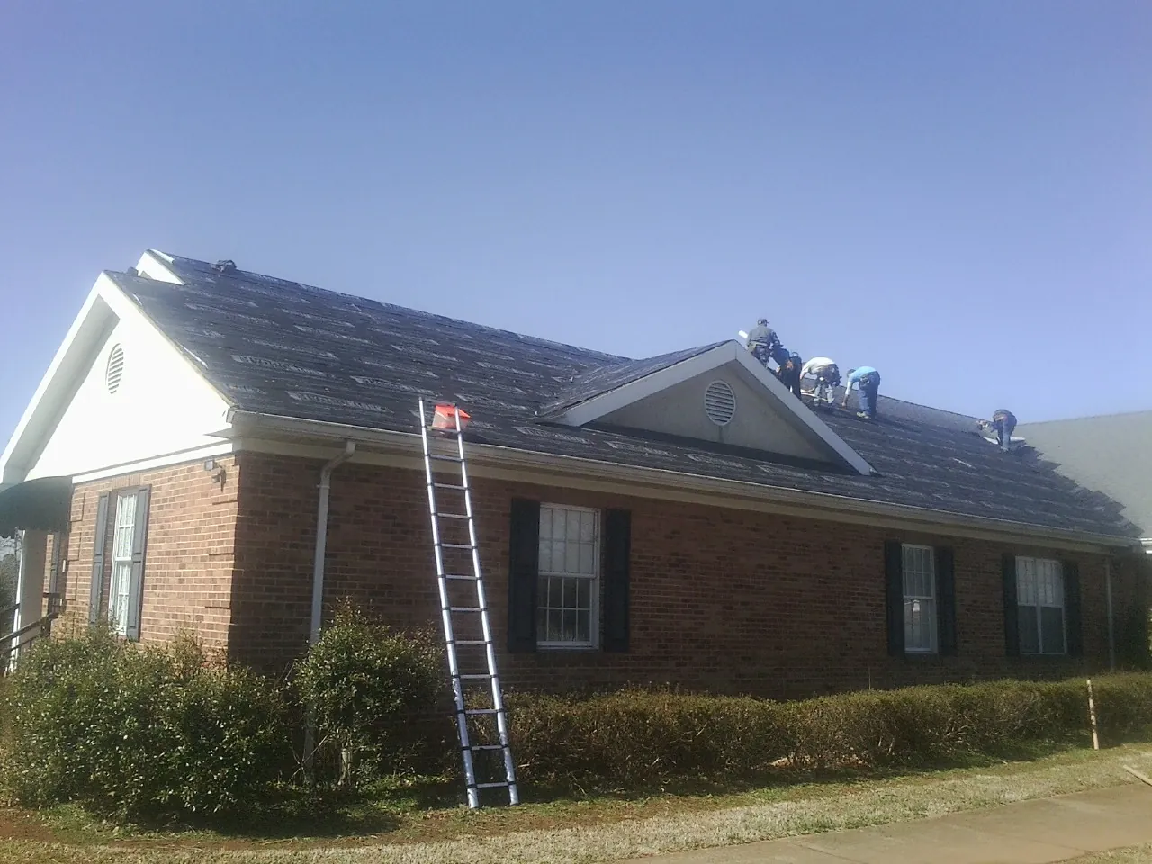 Crew tearing shingles off a brick ranch roof with a ladder set — Metal Roof Repair work by our crew in Chicago Heights