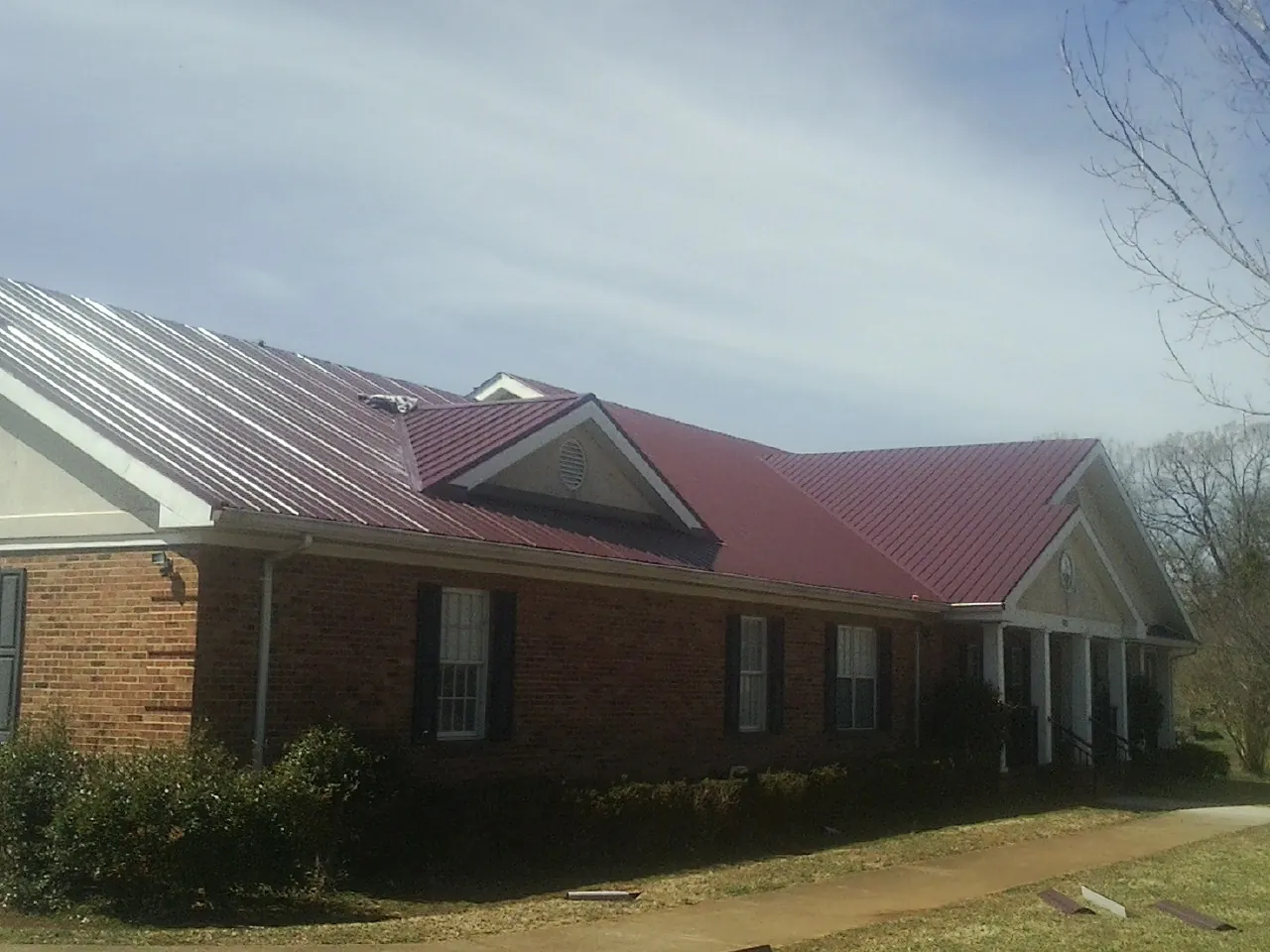 Red metal roof with gabled entries on a long brick building, from a Hail Damage Roof Repair job in Chicago Heights