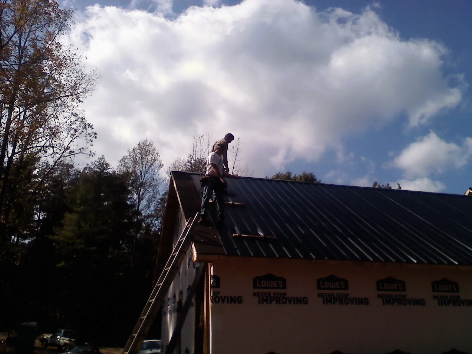Roofer fastening dark metal panels high against a cloudy sky, from a Roof Inspection job in Chicago Heights