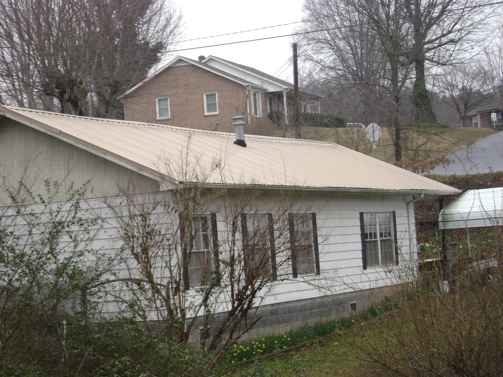 Tan metal roof on a white sided house set into a hillside — Commercial Roofing by Roofing Brothers in Chicago Heights